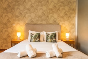 A hotel room with a large bed, two nightstands, two lamps, two pillows with a tropical print, and two rolled towels on the bed. - Funchal Frui Vita by Atlantic Holiday (Funchal)