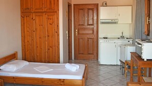 A room with two wooden beds, a kitchenette, and a wooden wardrobe. - Nikos Studio 2 in Gialiskari (Ikaria)