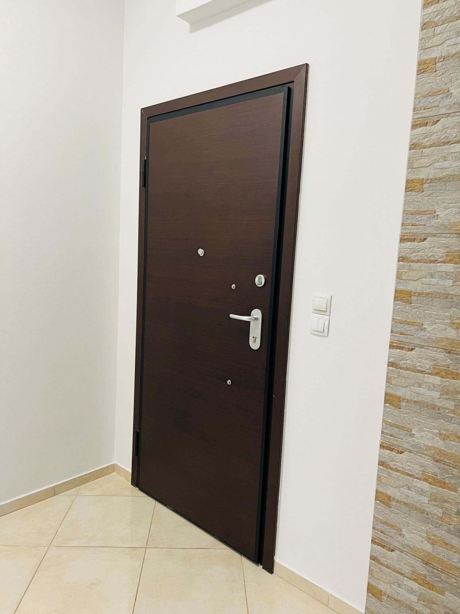 A closed dark wooden door with a handle and a lock, white wall, and a stone-textured wall to the right.