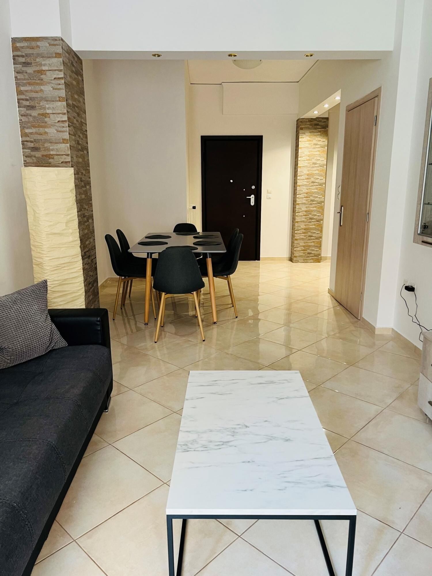 A modern living room with a dark sofa, a marble coffee table, and a dining area with a table and chairs.