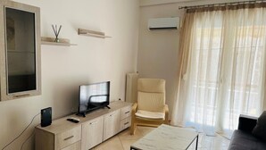 A modern living room with a flat-screen TV on a wooden cabinet, a beige armchair, a small table, and a large window with sheer curtains. - Piraeus 3 in Piraeus (Piraeus)