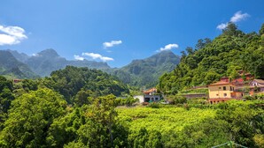 A rural landscape with a house surrounded by lush greenery and mountains in the background. - Vila do Largo B by Homie (São Vicente)
