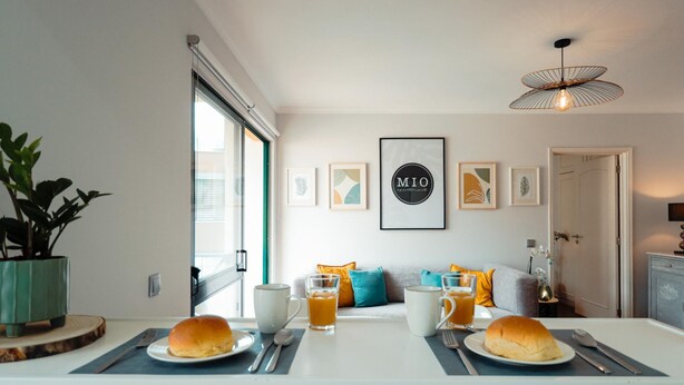 A modern kitchen with a dining table set for two, a potted plant, and framed artwork on the wall. - MIO Apartment by Homie (Funchal)