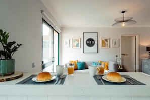 A modern kitchen with a dining table set for two, a potted plant, and framed artwork on the wall.