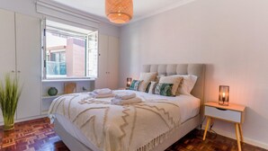 A bedroom with a bed, bedside table, lamp, window, and a potted plant. - MIO Apartment by Homie (Funchal)