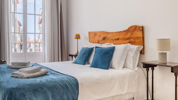 Una camera d'albergo con un letto grande, una testiera in legno, una vista dalla finestra e un comodino con una lampada.