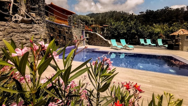 A pool area with a stone wall, lounge chairs, and a small building. - Casas Maravilha - Rvore by Homie (Calheta)