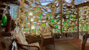 A room with stone walls, wicker chairs, and a unique wall decoration of various bottles. - Casas Maravilha - Rvore by Homie (Calheta)