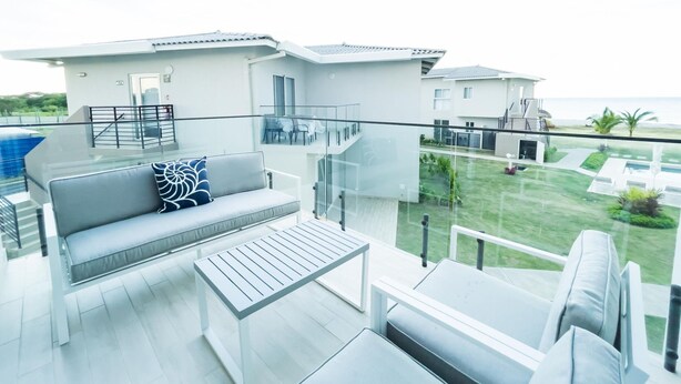 Varanda moderna ao ar livre com sofá, mesa e vista para a piscina.