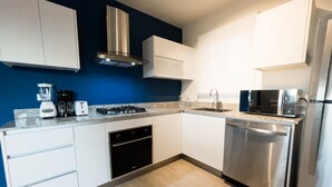 Uma cozinha moderna com armários brancos, lava-louças de aço inoxidável, micro-ondas, fogão a gás e forno embutido.