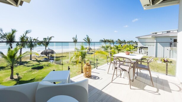 Un balcone con vista sulla spiaggia, arredi da esterno e ringhiera in vetro.