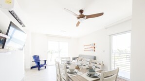 Una luminosa sala da pranzo con tavolo in legno apparecchiato per quattro persone, una ventola a soffitto e vista all'esterno attraverso ampie finestre.