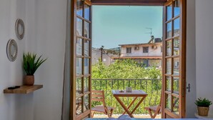 Een balkon met een bed, een tafel en stoelen, met uitzicht op een woonwijk.