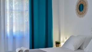 Een hotelkamer met een bed, twee opgerolde handdoeken, een potplant en een decoratieve spiegel aan de muur.