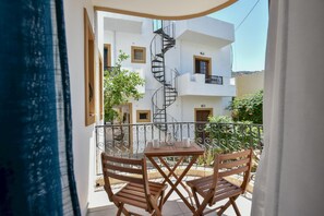 A balcony with a table and chairs, a spiral staircase, and white buildings in the background.