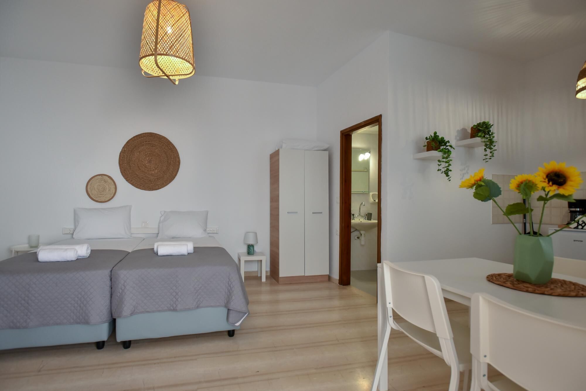 Une chambre d’hôtel avec deux lits, un bureau, une chaise, un luminaire suspendu et une vue sur la salle de bain.
