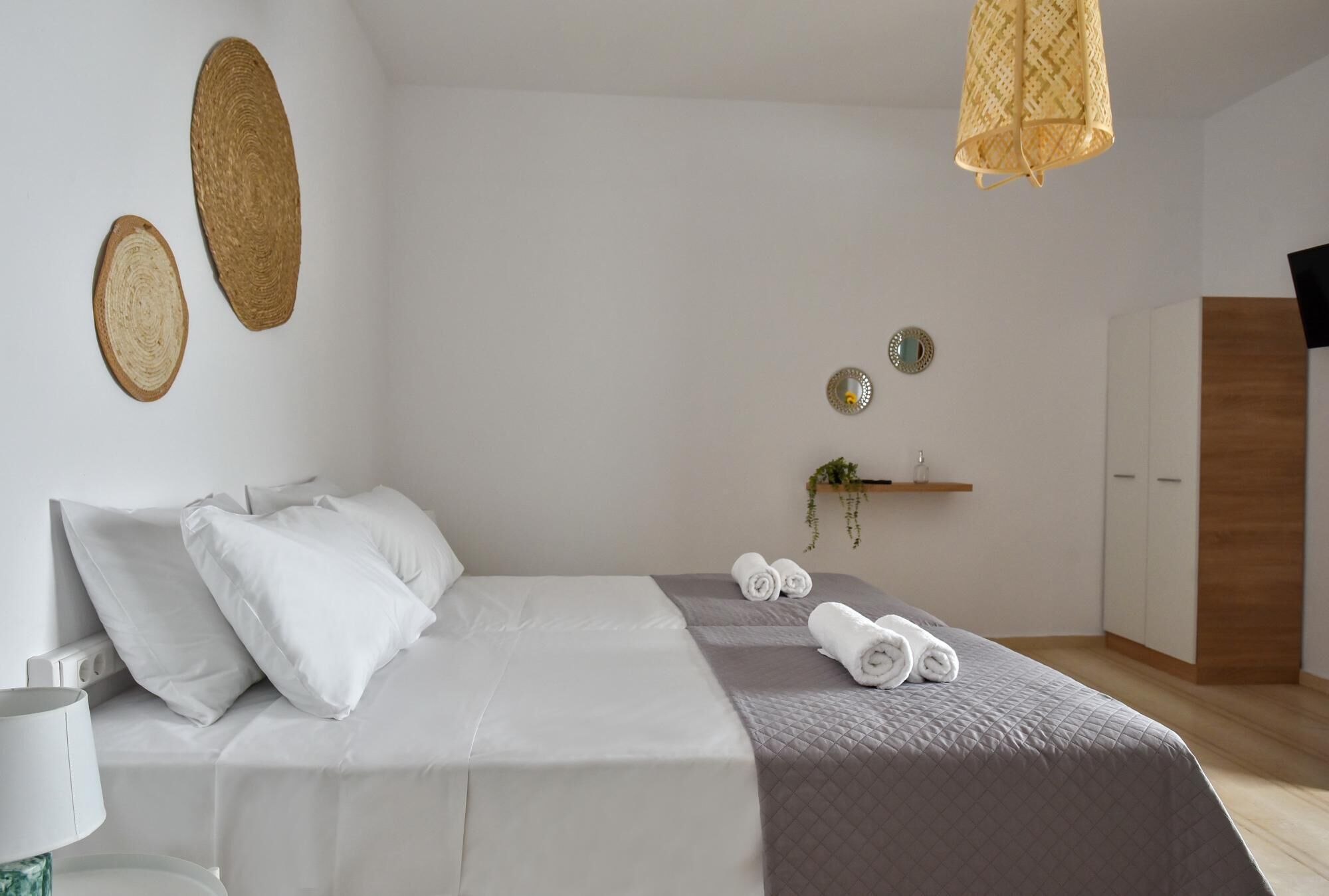 A neatly made bed with white and gray bedding, a hanging light fixture, and a wooden wardrobe.