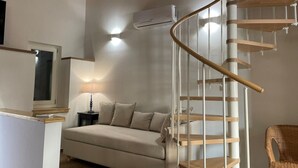 Un salon moderne avec un canapé beige, une lampe, un fauteuil en osier et un escalier en colimaçon.