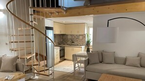 Un salon moderne avec un escalier en colimaçon, un canapé, une table en bois et, au fond, un coin cuisine.