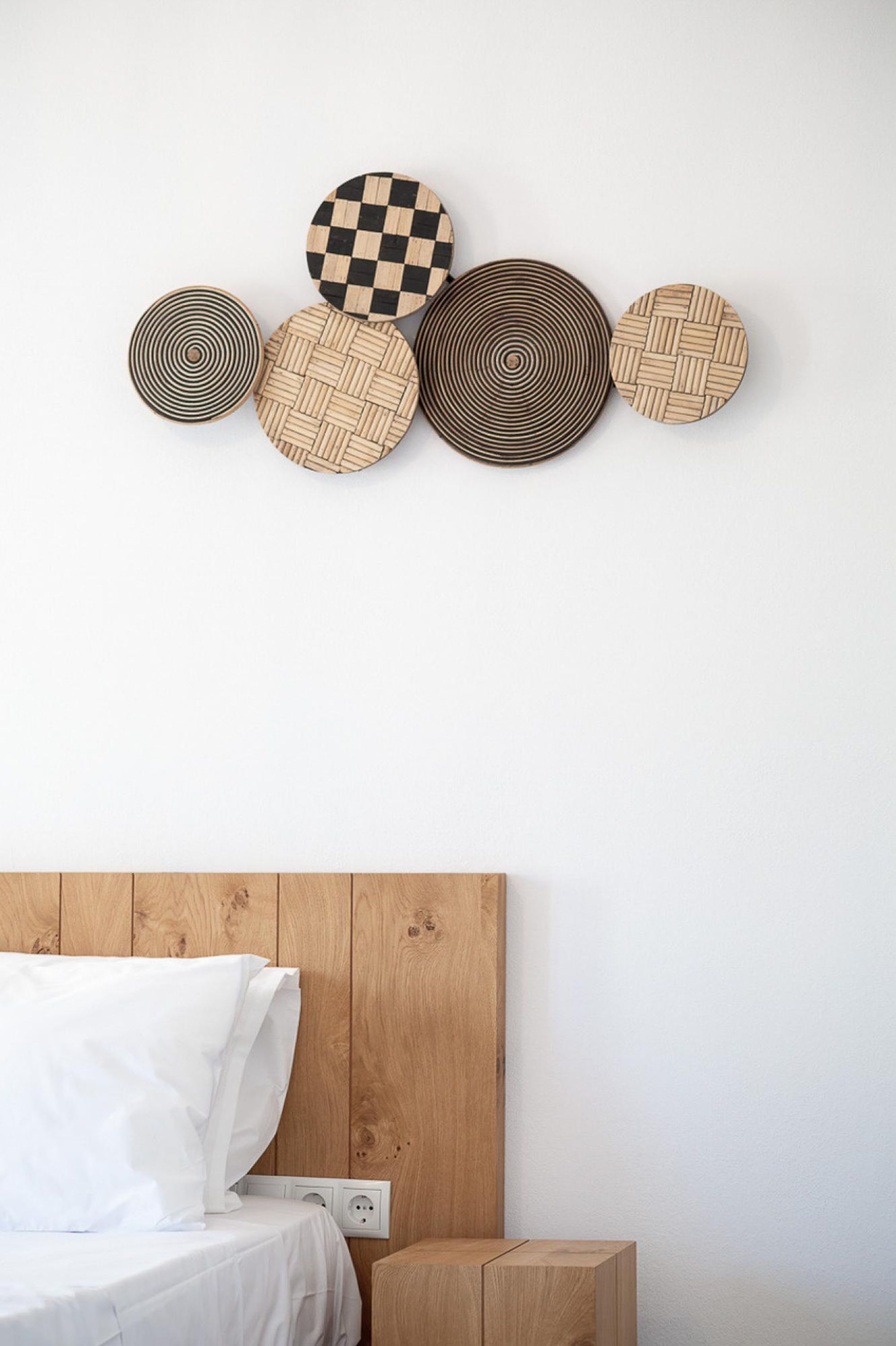 Camera da letto con testiera in legno, letto con biancheria bianca e un'opera d'arte circolare in legno appesa al muro.