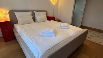 Un lit parfaitement fait, avec du linge de lit et des serviettes blanches, une tête de lit moderne et un luminaire mural original.