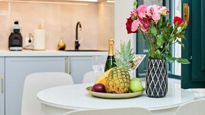 A dining table with a fruit bowl containing pineapple, apple, and grapes, a bottle of champagne, and a vase with flowers. - Exquisite Villa by Dominium - Old city (Dubrovnik)