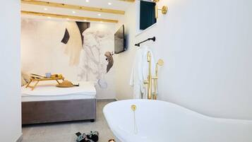 Ein modernes Badezimmer mit freistehender Badewanne, Holzboden und einem an der Wand montierten Fernseher.