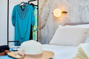 A bedroom with a bed, a wall-mounted light, and a clothing rack with a blue garment.