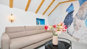 A modern living room with a beige sofa, a glass coffee table with a vase of flowers, and a large abstract painting on the wall. - Exquisite Villa by Dominium - Old city (Dubrovnik)