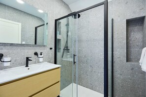 A modern bathroom with a glass-enclosed shower, a white sink, and a marble-tiled wall.