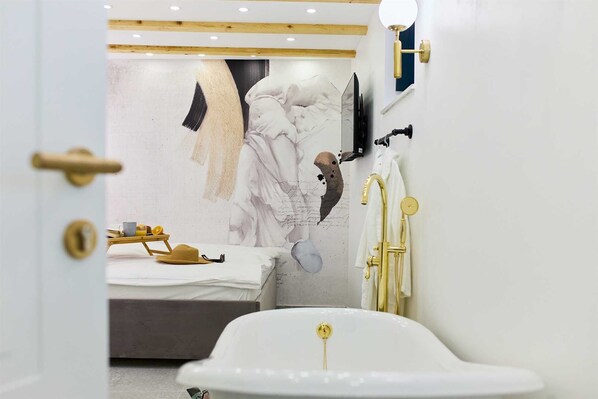 A modern bathroom with a white bathtub, a gold faucet, and a marble wall with a painting.