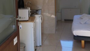 A compact hotel room with a kitchenette, a bed with towels, and a window with a view of trees. - DUBROVNIK HAUS suites Standard studio apartment (Dubrovnik)