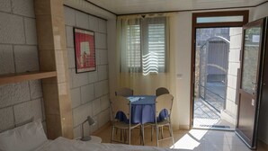 A hotel room with a bed, a small table with chairs, a window with blinds, and a door leading to a balcony. - DUBROVNIK HAUS suites Standard studio apartment (Dubrovnik)