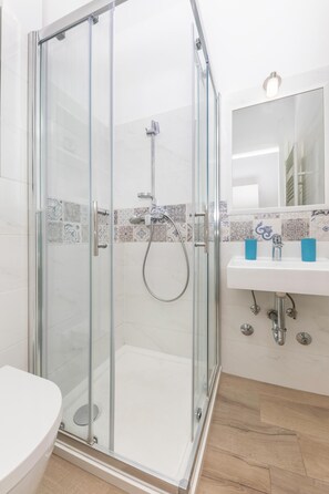 A bathroom with a glass shower enclosure, a white sink with two blue soap dispensers, and a mirror above the sink. - Modern Studio Near Park Zrinjevac and Main Square (Zagreb)