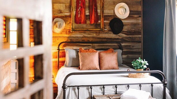 Une chambre à coucher au style rustique, avec un plafond en bois, un cadre de lit en métal et une vieille malle servant de table de chevet.