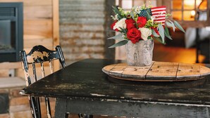 Un coin repas rustique avec une table en bois, des chaises et un vase orné de fleurs et d’un drapeau américain.