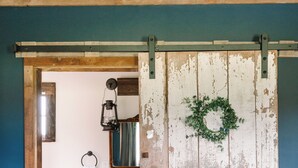 Un baño rústico con puerta de madera, un farol colgante, una toalla blanca y un balde pequeño.