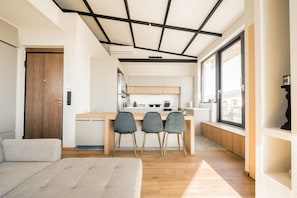 A modern kitchen with a central island, wooden flooring, and a large window offering a view. - Sky Apartment in Dafni (Dafni-Ymittos)