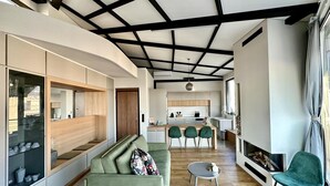 Ein modernes Wohnzimmer mit einer Couch, einem Couchtisch und einem Kamin. Im Hintergrund ist eine Küche mit Essbereich zu sehen.