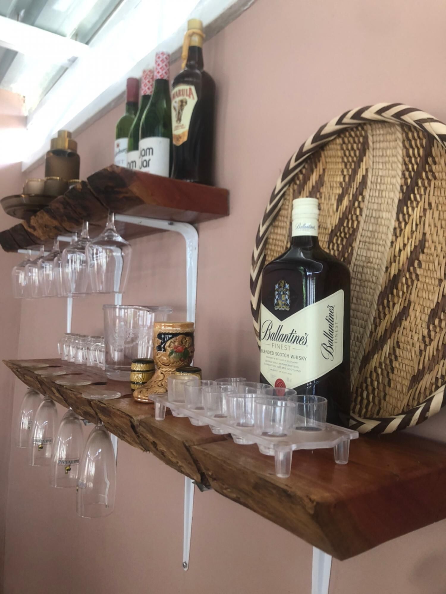 Een bar met een houten plank waarop een fles Ballantine's whisky, glazen en decoratieve voorwerpen staan.