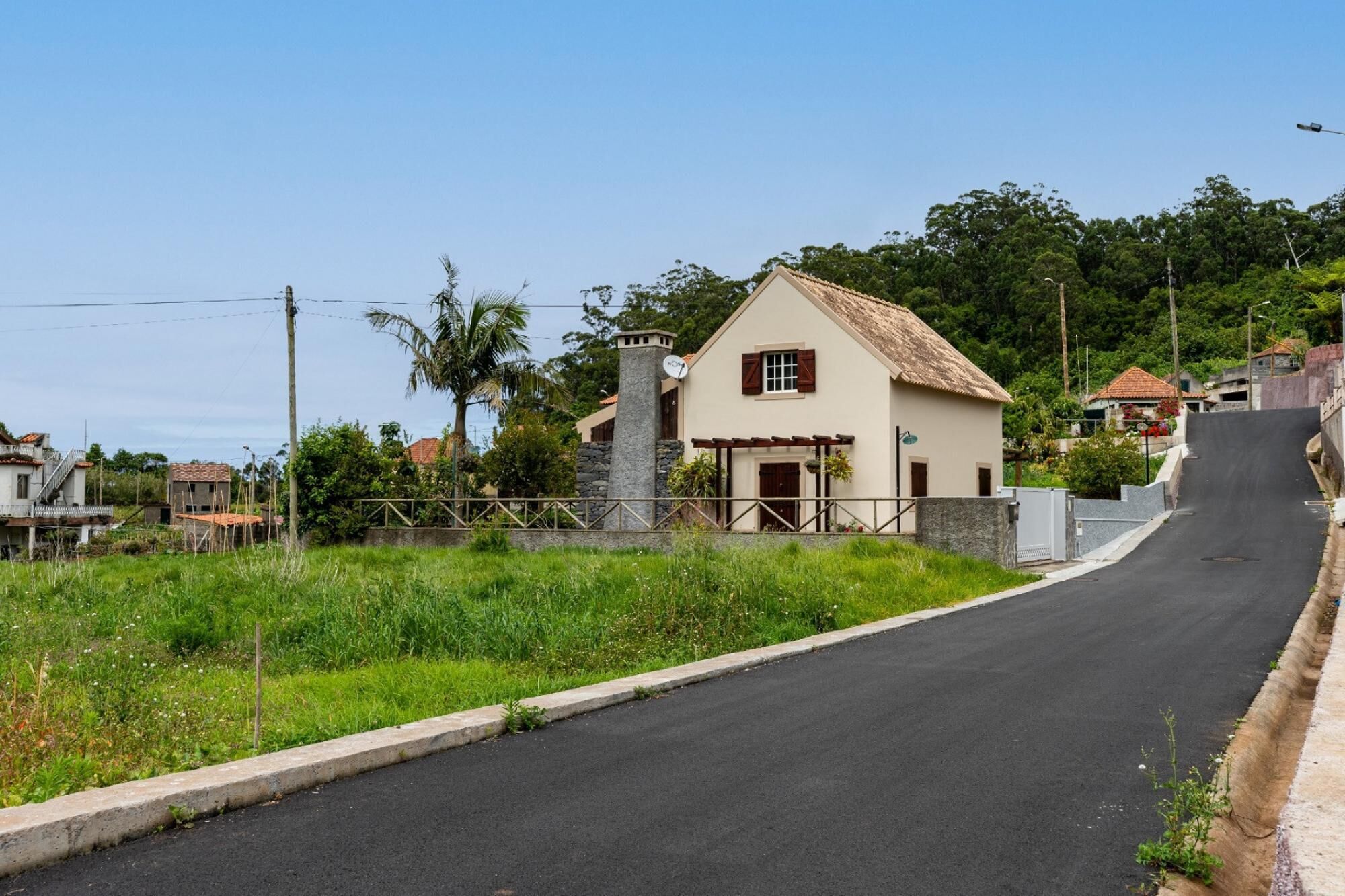 A rural road leading to a white house with a tiled roof and a stone chimney.