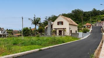 A rural road leading to a white house with a tiled roof and a stone chimney.