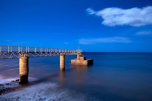 A bridge over calm water at night with a clear sky. - Madalena Sunset by Homie (Ponta do Sol)