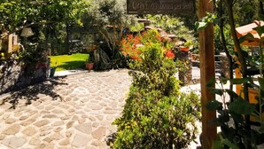 Caminho no jardim que leva a uma área de descanso, com uma placa indicando que está aberto 24 horas por dia.