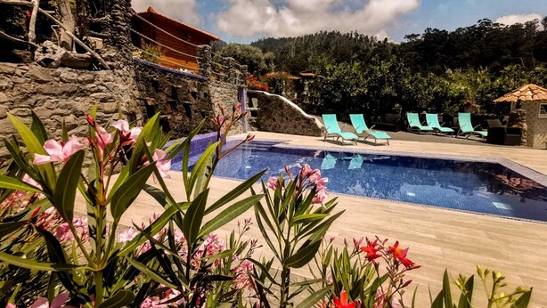 Uma área de piscina com muro de pedra, espreguiçadeiras e um pequeno edifício.
