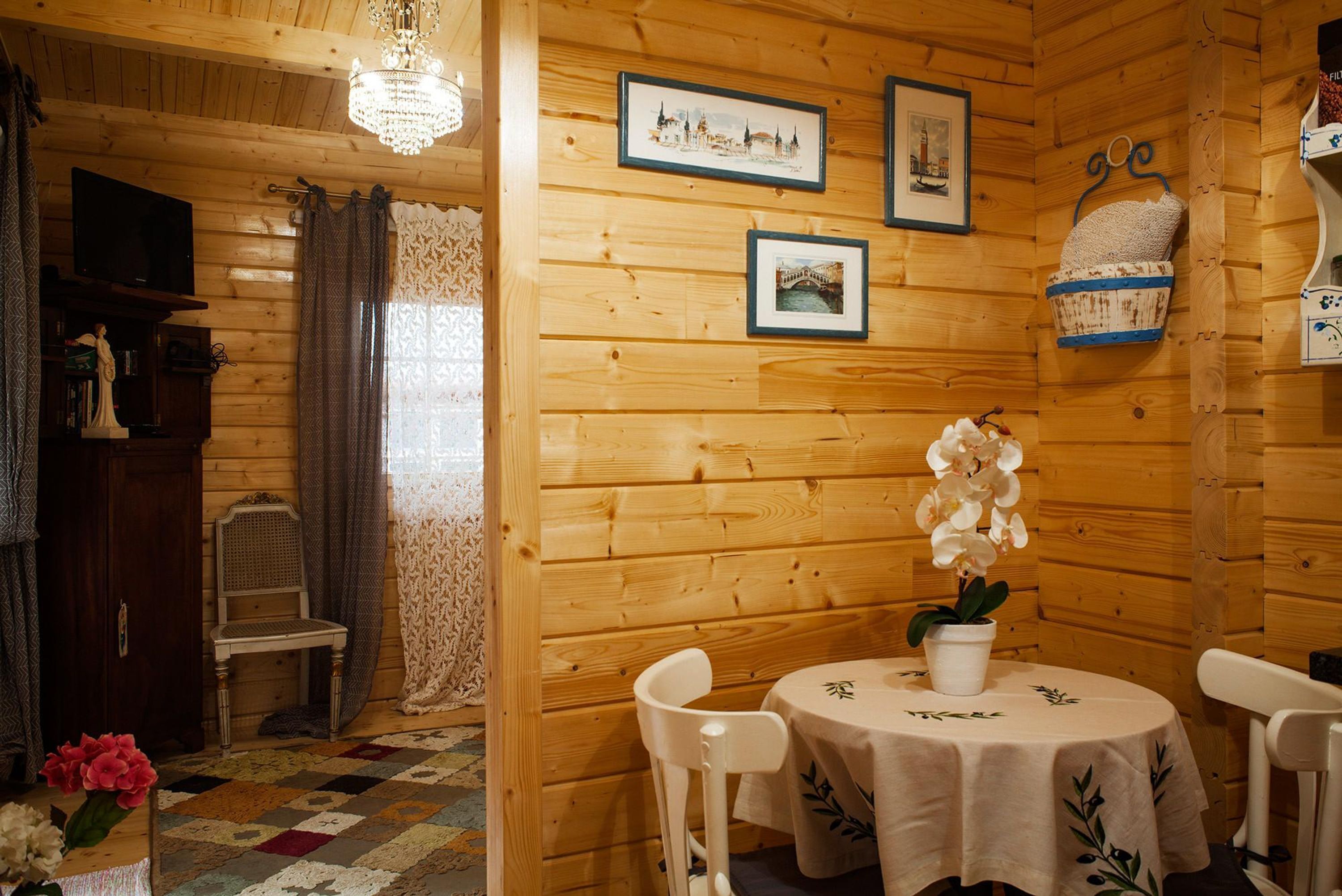 Interior de una cabaña de madera con una mesa de comedor, sillas, un candelabro, cuadros enmarcados y una cesta en la pared.