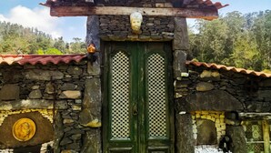 Um edifício rústico de pedra com uma porta verde, telhado de telhas e uma parede de pedra com um emblema circular.