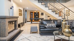 Ein modernes Wohnzimmer mit Kamin, einem schwarzen Ledersofa, einem Glastisch und einer Treppe mit Metallgeländer.