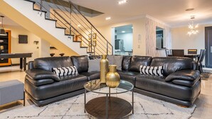 Ein modernes Wohnzimmer mit einem schwarzen Ledersofa, einem Glastisch und einer Treppe mit Metallgeländern.