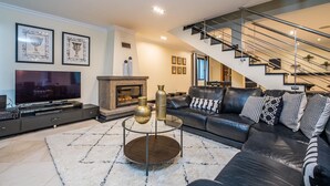 Ein modernes Wohnzimmer mit Kamin, großem Flachbildfernseher, Ledersofa und einer Treppe.